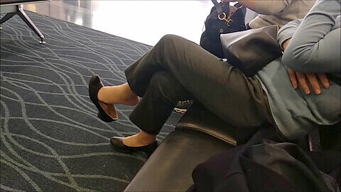 Elderly Asian woman in glasses takes off sexy flats and candidly dangles them in airport, revealing unpainted toes