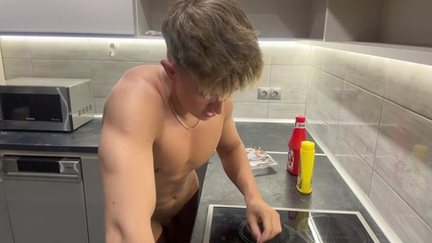 Bel ragazzo biondo prepara un delizioso banchetto nudo in cucina